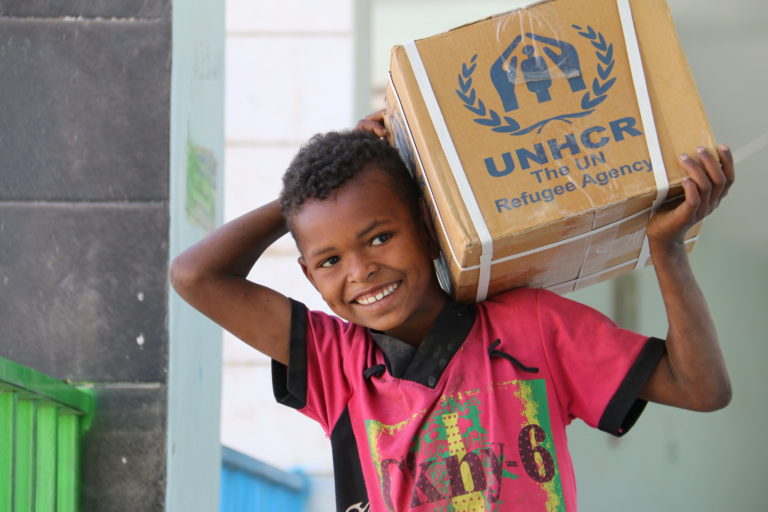 Barn bär förnödenheter från UNHCR på axeln